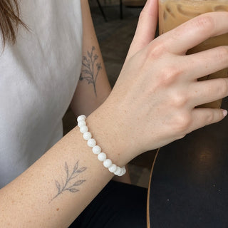 Jade bead bracelet worn on a tattooed forearm holding a coffee