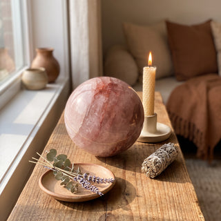 Hematoid Quartz Sphere Unique #4 - 3 3/4" displayed on a wooden home altar shelf beside a candle, shown at true size in warm natural light.