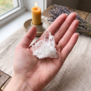Small clear quartz cluster resting in an open palm above a linen-covered wooden altar with a beeswax candle and dried lavender