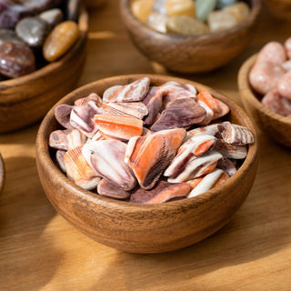 Mano De Lion Orange Shell Tumbled Stones in a wooden bowl on a boutique display table