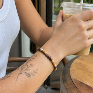 Mookaite Jasper bead bracelet worn on a tattooed forearm holding a coffee