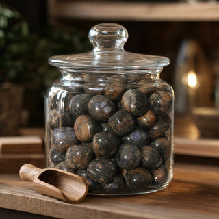 Que Sera Tumbled Stones in a glass apothecary jar with a scoop