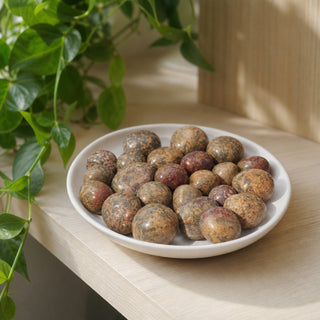 Red Leopardskin Jasper Tumbled Stones in a stoneware dish on a shop shelf
