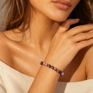 Rhodochrosite bead bracelet worn with the fingertips resting at the collarbone