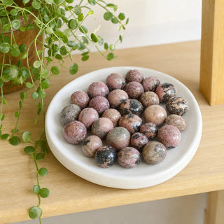 Rhodonite Dark Tumbled Stones in a stoneware dish on a shop shelf