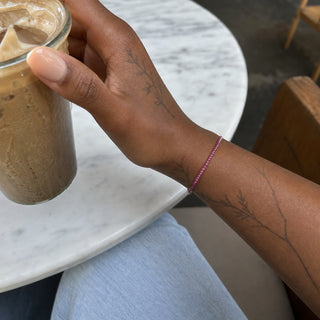 Ruby bead bracelet worn on a tattooed forearm holding a coffee