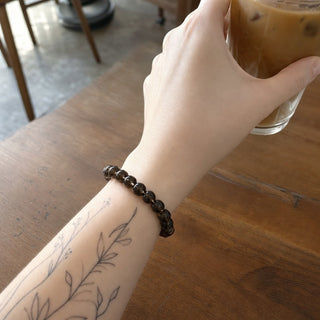 Smoky Quartz bead bracelet worn on a tattooed forearm holding a coffee