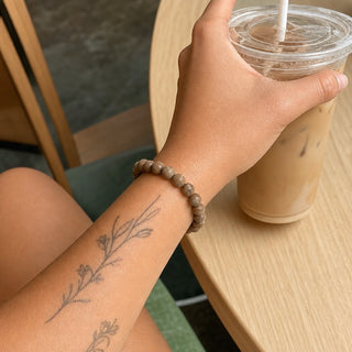 Wood Jasper bead bracelet worn on a tattooed forearm holding a coffee